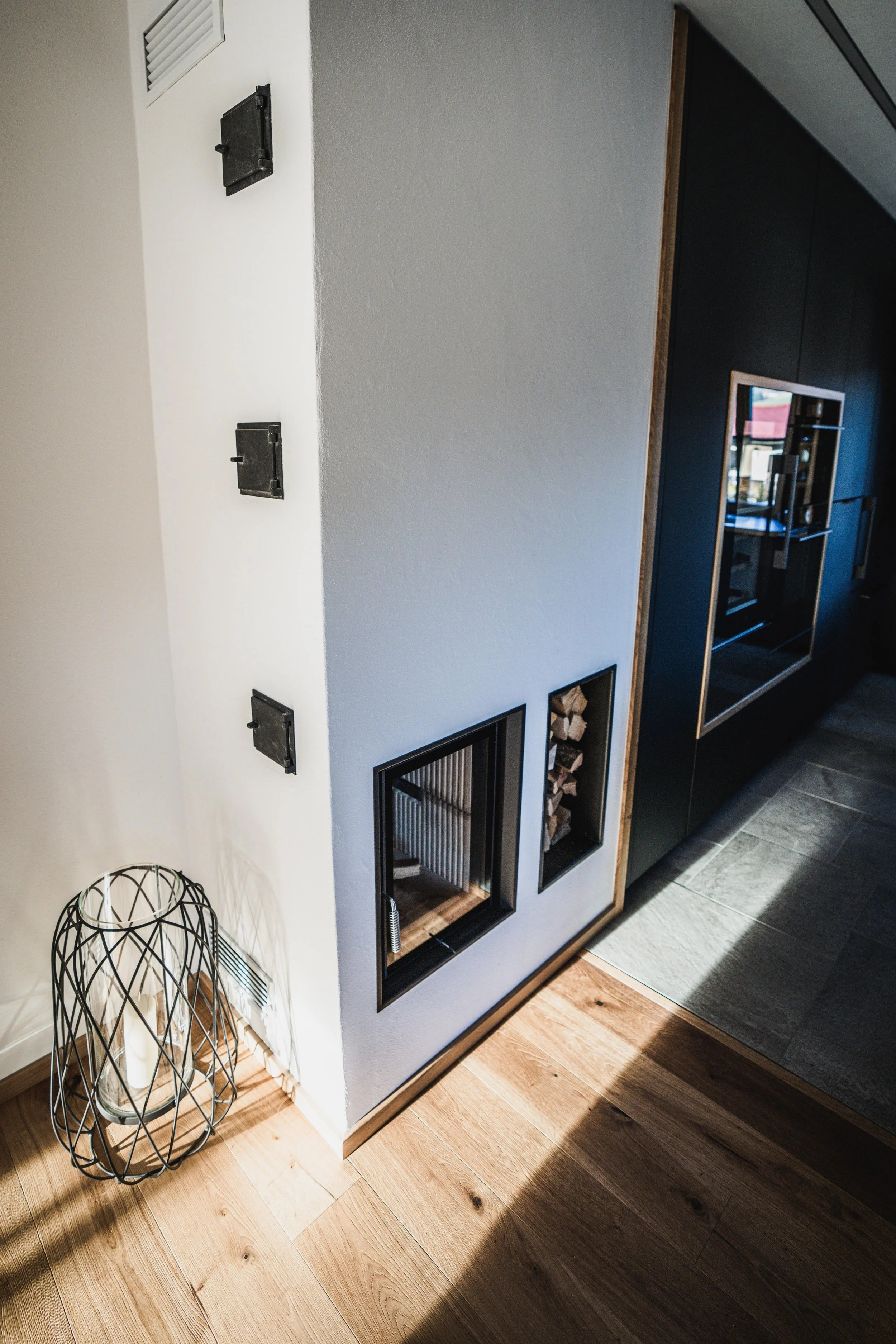 Innenaufnahme eines Hauses mit Holzfußboden, Wand mit Holzregal, Kamin, Holzlager und Stromanschlüssen.