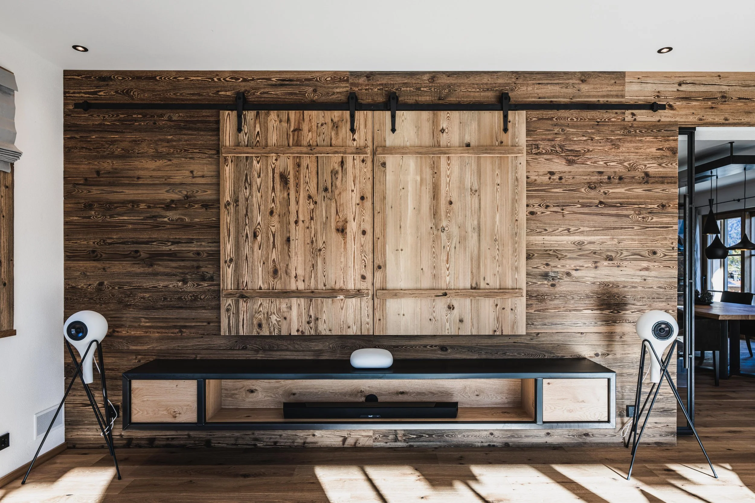 Moderner Wohnzimmerbereich mit Holzverkleidung, einer schwarzen TV-Konsole, Lautsprechern und einem Kunstobjekt auf der Konsole.