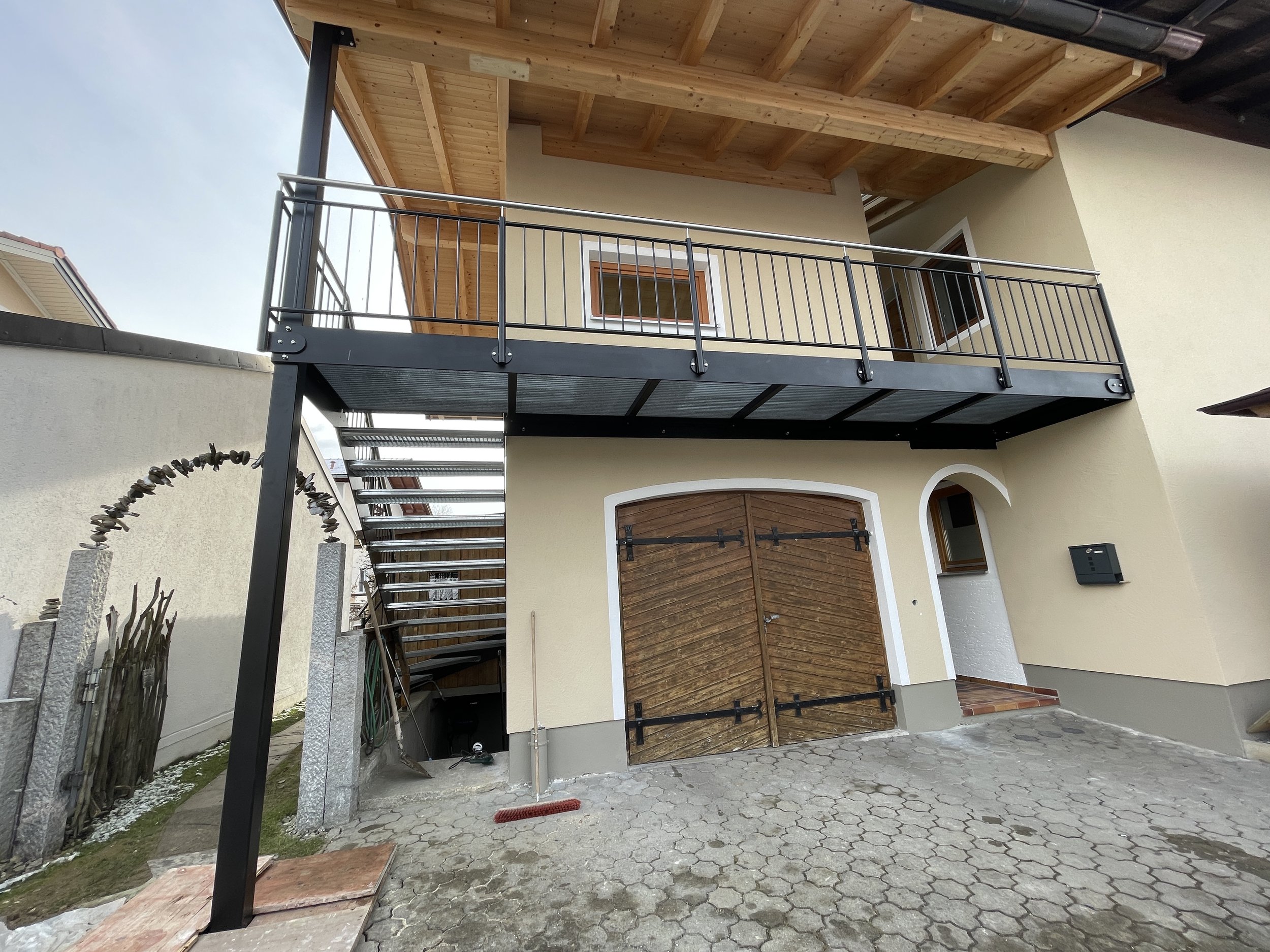 Mehrstöckiges Haus mit gelber Fassade, Holztüren, Balkon und Metalltreppe im Außenbereich.