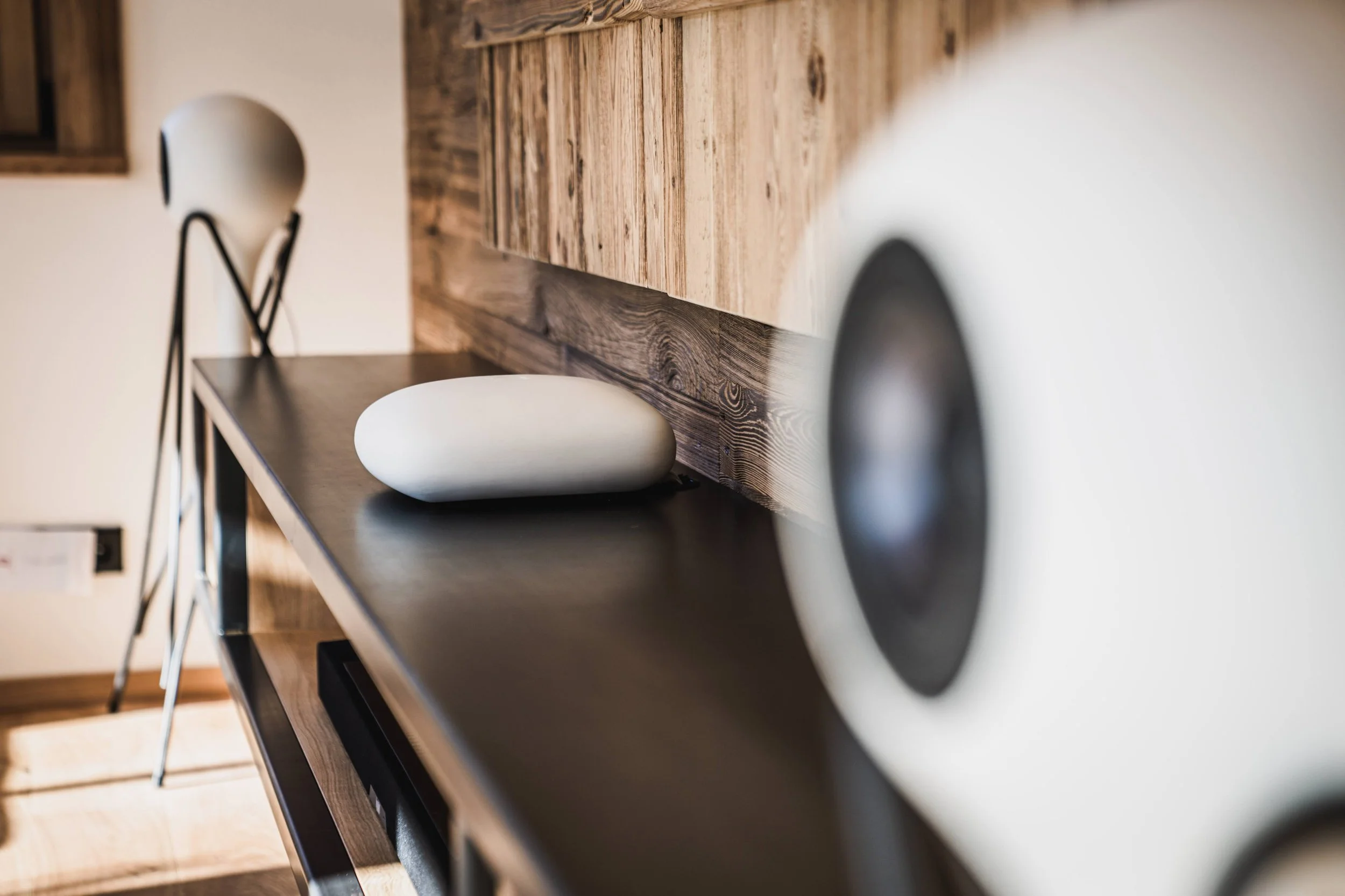 Nahaufnahme einer schwarzen Küchenarbeitsplatte mit einem weißen dekorativen Gegenstand, im Hintergrund eine weiße Lampe mit schwarzem Gestell und Holzmöbel