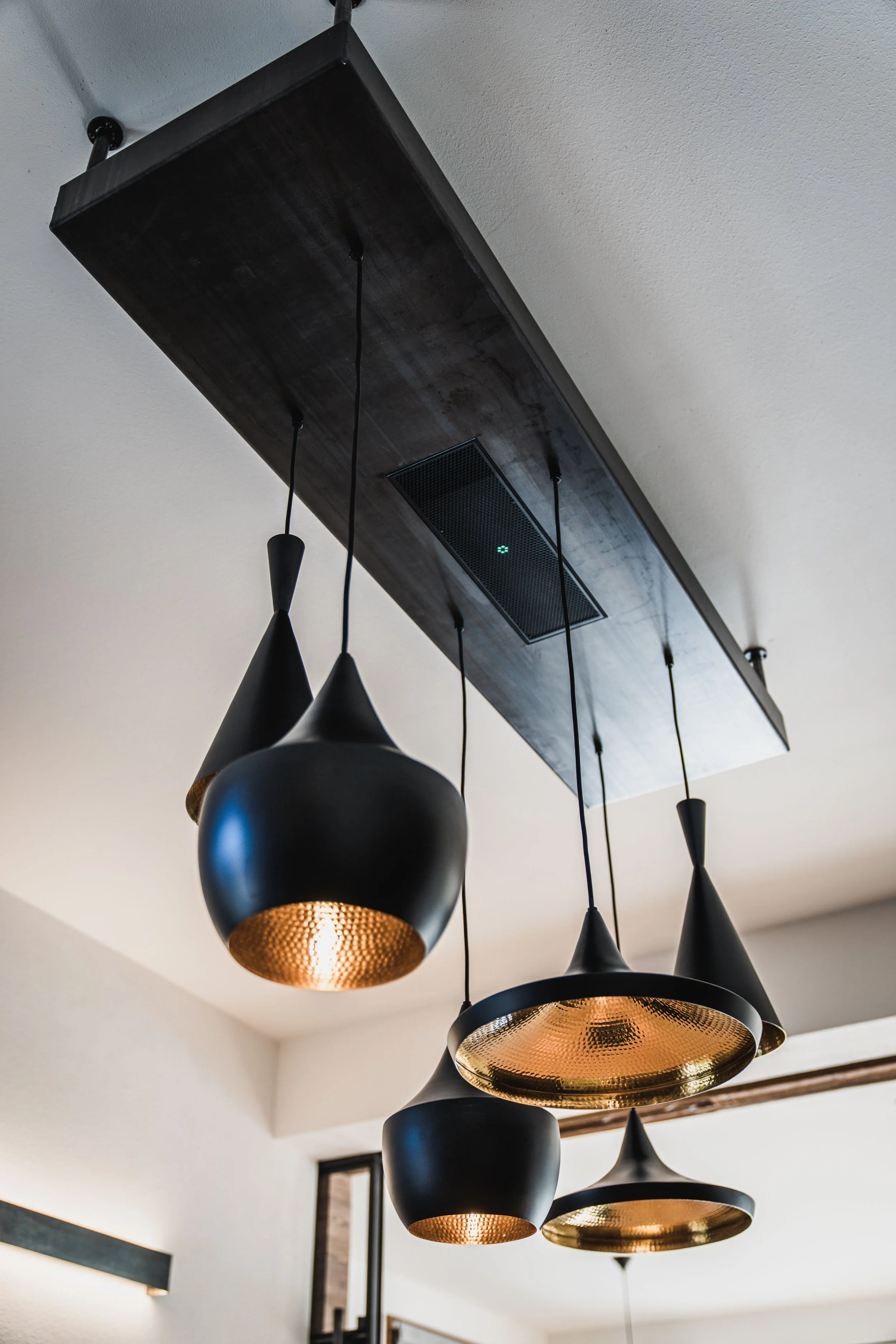 Moderne schwarze Hängeleuchte mit goldener Innenseite, an geschwungenen Kabeln von einer schwarzen Holzdecke in einem Wohnzimmer.