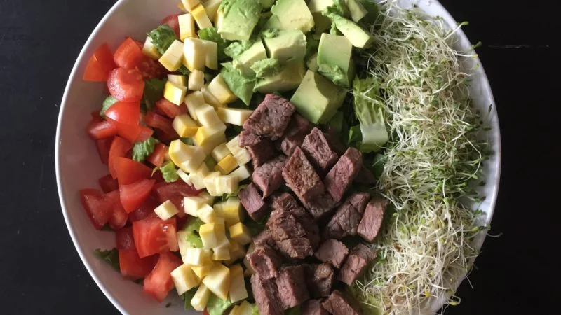 Spring steak salad with tomato, squash, avocado, sprouts and steak.