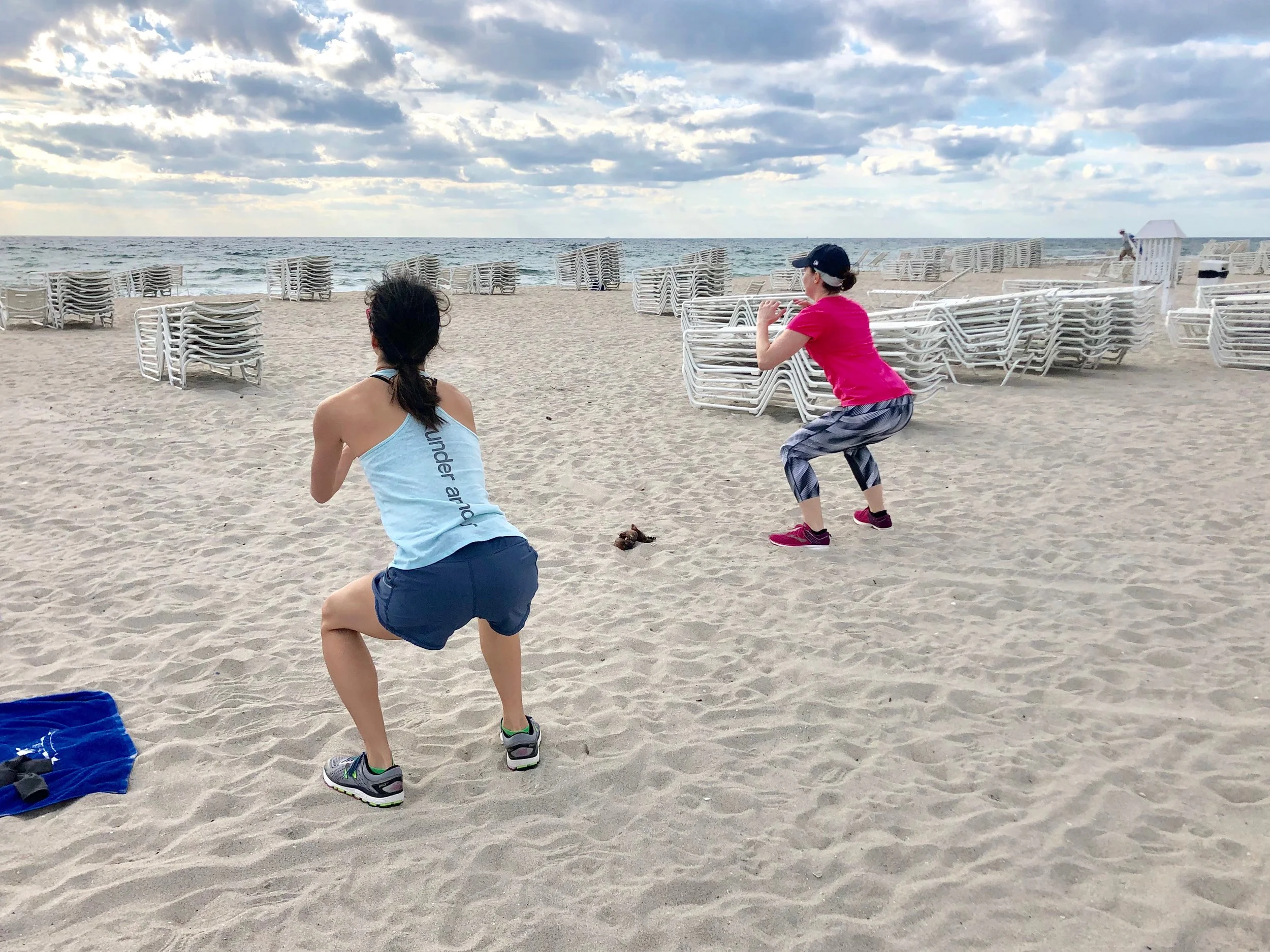 Boot camp guests do squats on the beach during bodyweight workout.