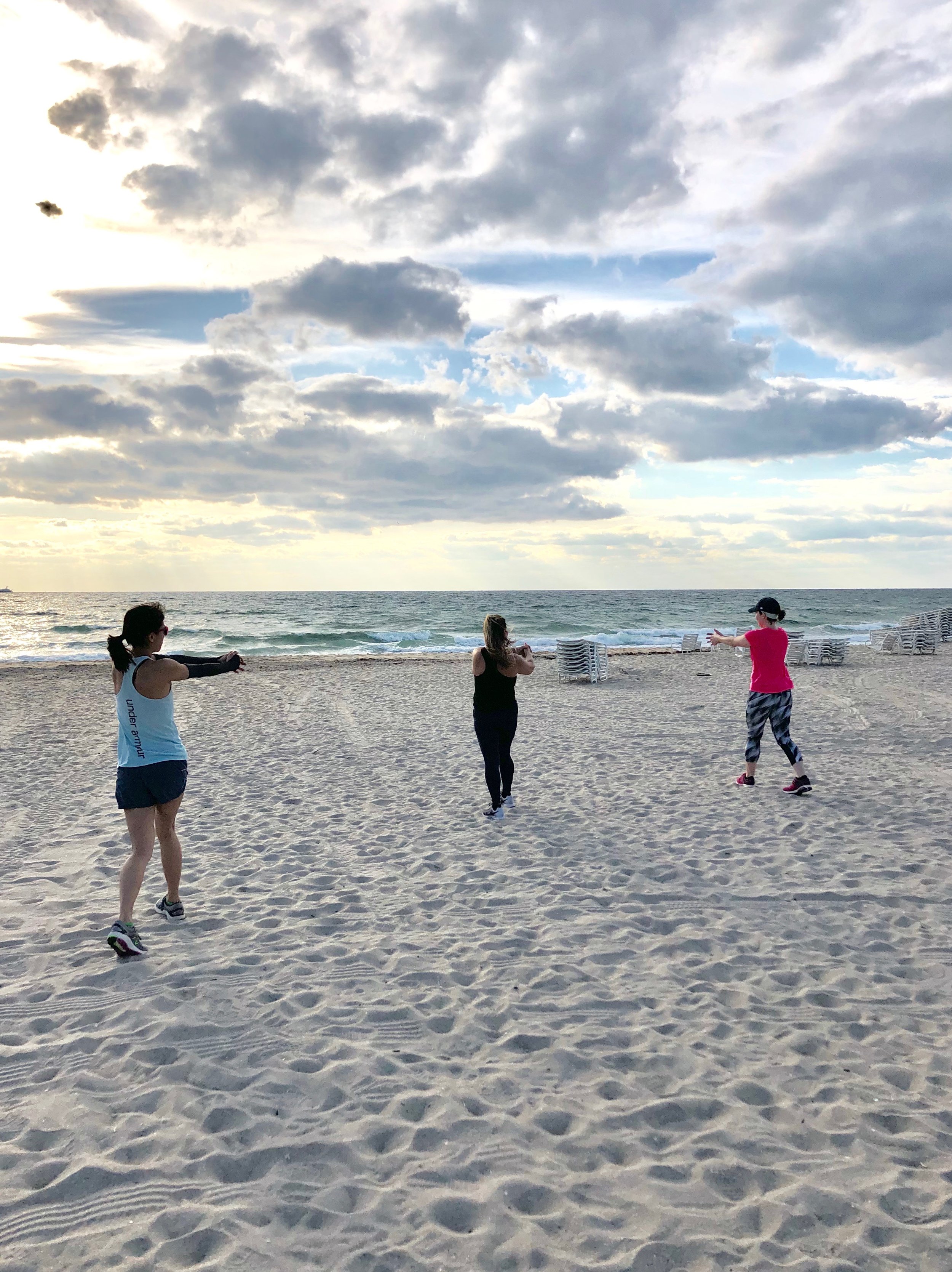 Boot camp guests workout on beach during fitness vacation.