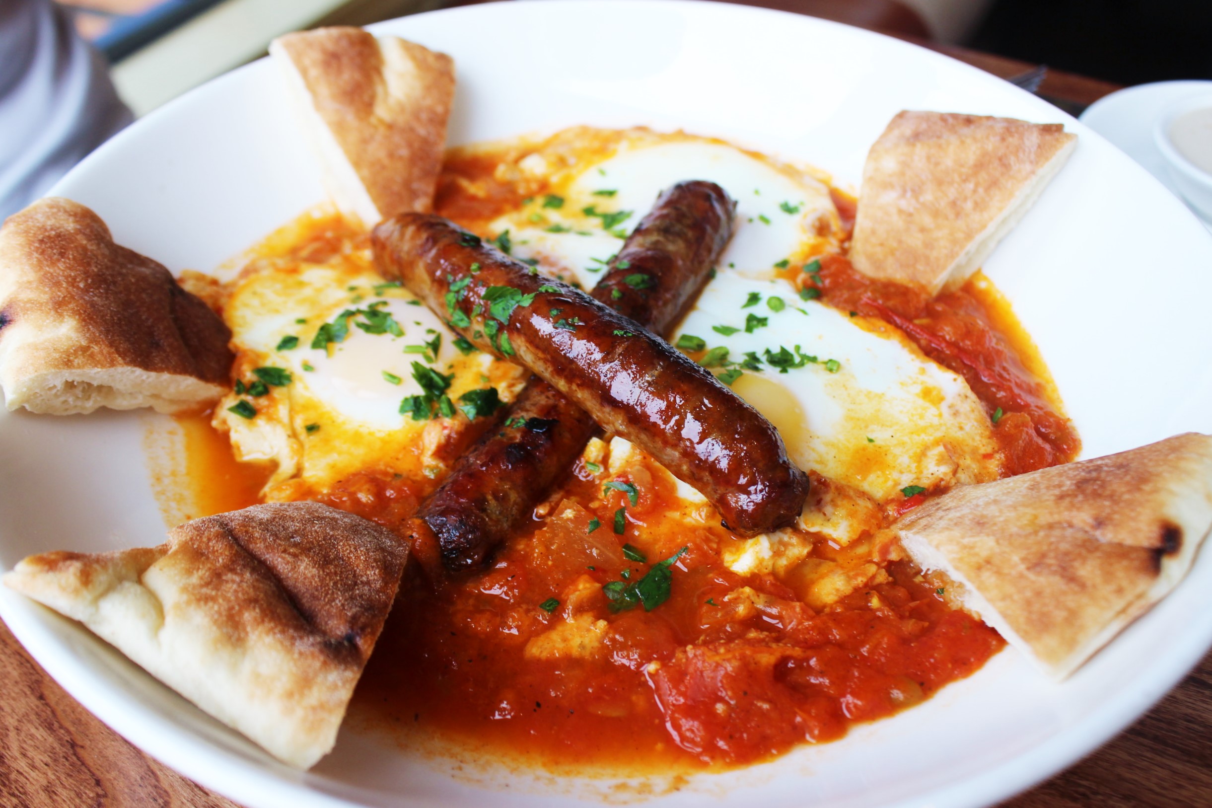 Shakshuka Moroccan Breakfast: three eggs baked with tomato, onion, pepper, spices, tahini, pita, and merguez sausage