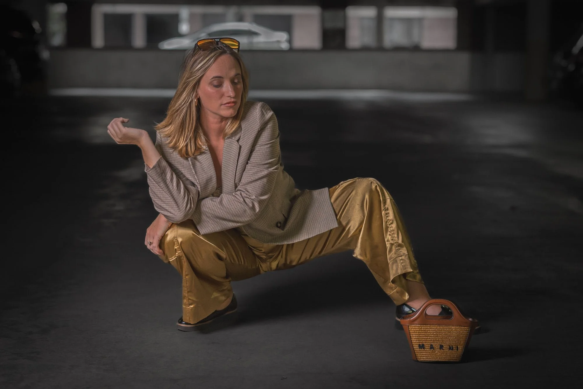 A woman in a blazer and gold pants poses squatting in a dimly lit garage—personal branding photography at its boldest.