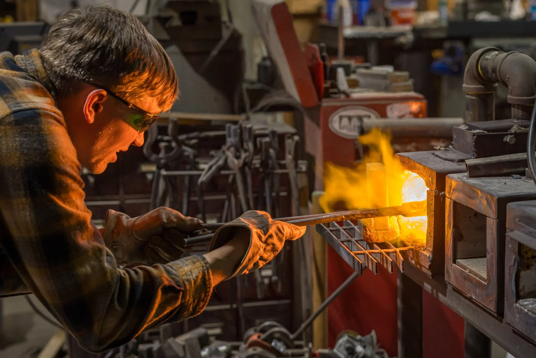 Industrial Photographer Richmond - An industrial photographer in Richmond captures a man in safety glasses heating metal amid bright flames and forge tools.