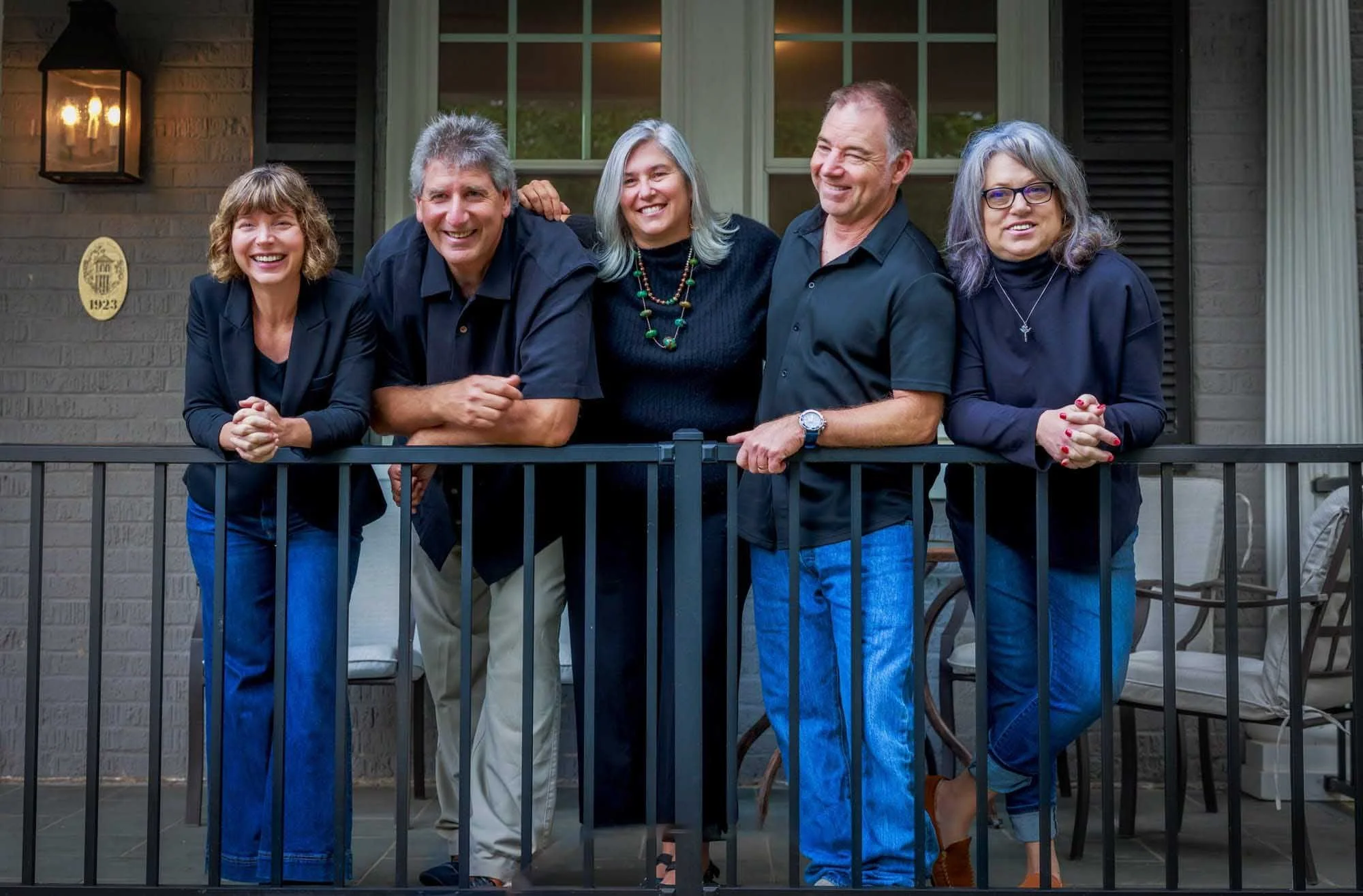 Five adults stand and smile on a porch, all in black tops and blue jeans—a great example of a Lifestyle brand session