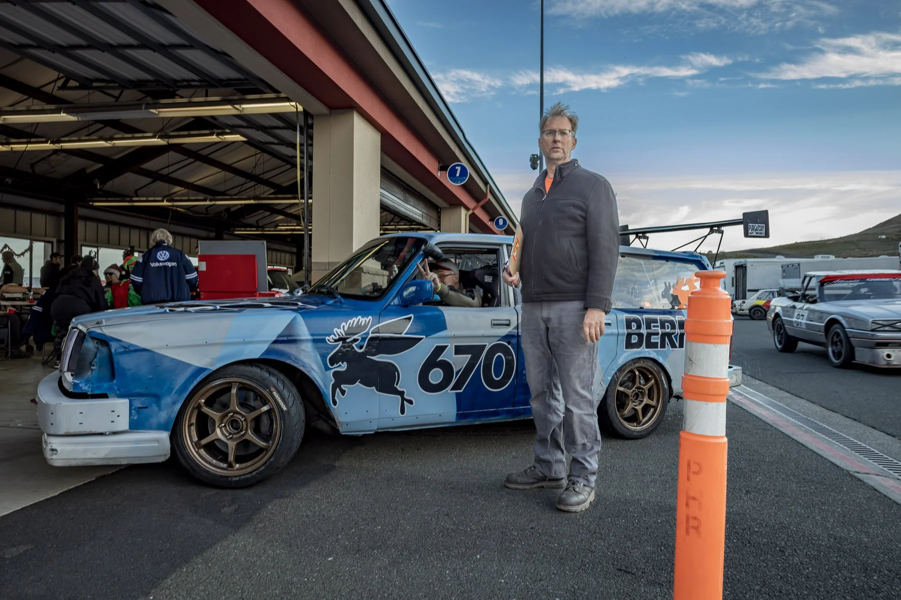 Industrial Photographer Richmond - An industrial photographer Richmond captures a man by a blue race car #670 with a moose graphic, parked near the track garage.