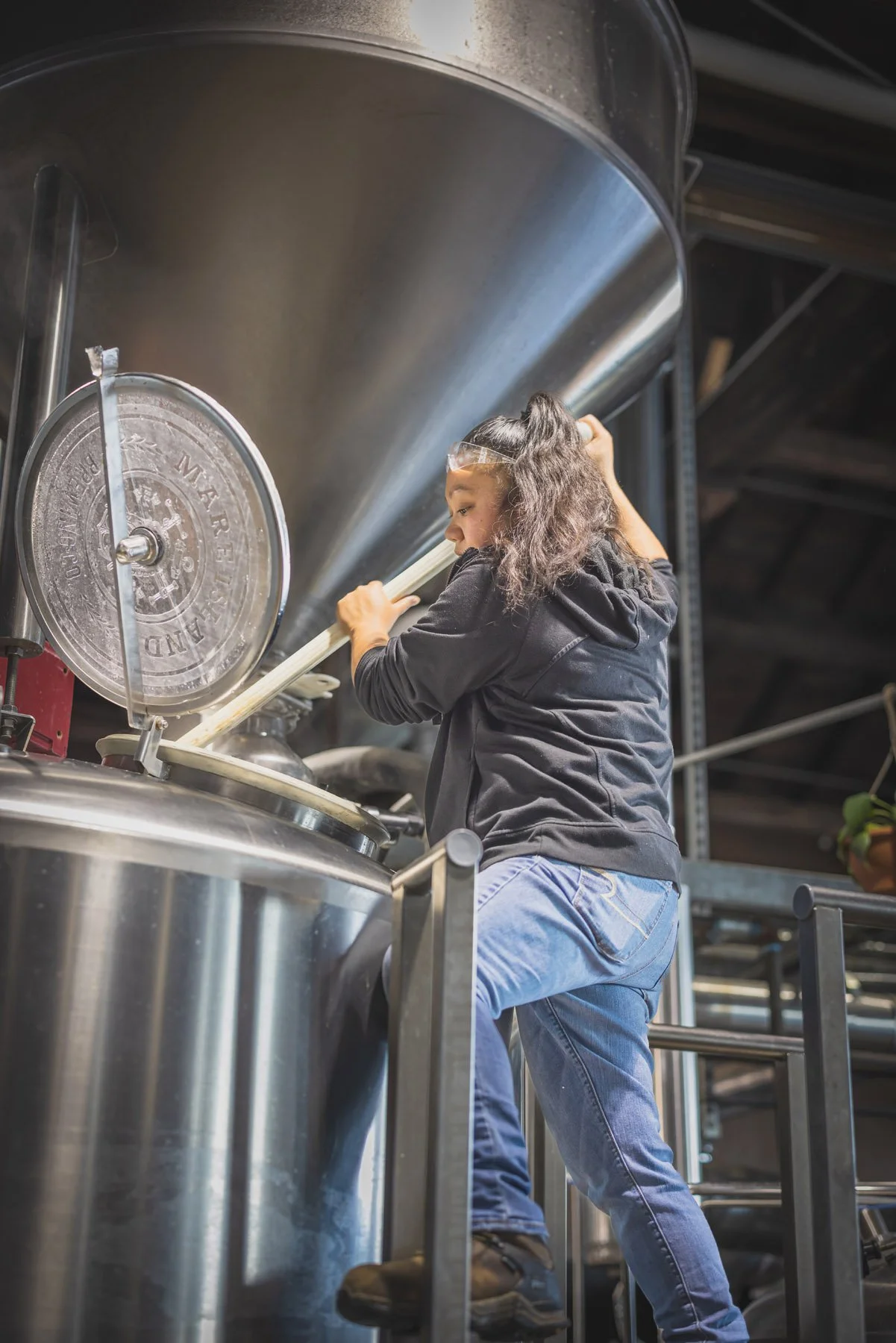 Industrial Photographer Richmond - An industrial photographer Richmond captures a woman stirring inside a large stainless steel brewing tank on a platform.