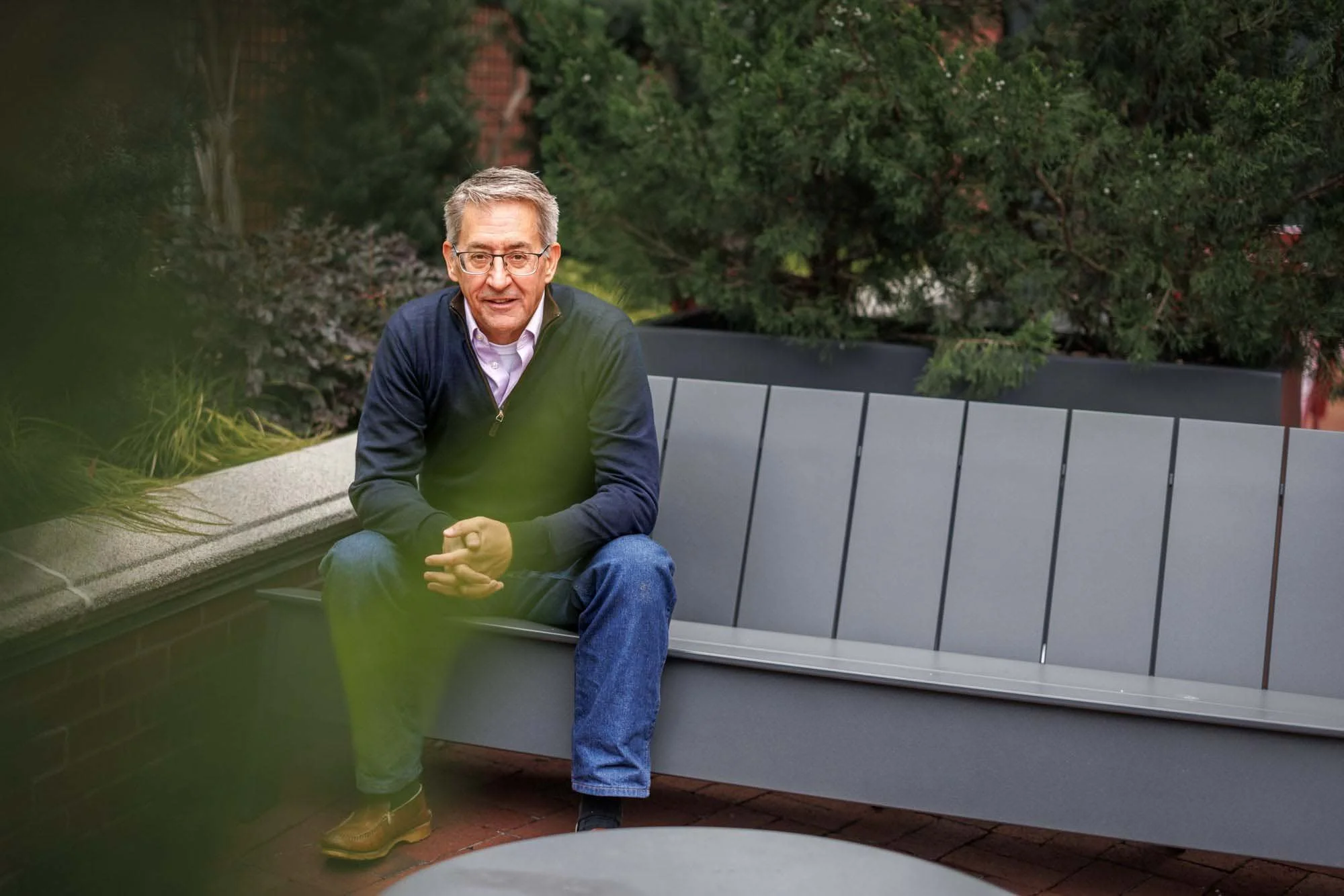 A man in glasses and a dark sweater sits on a gray bench outdoors—an ideal scene for a Lifestyle brand session