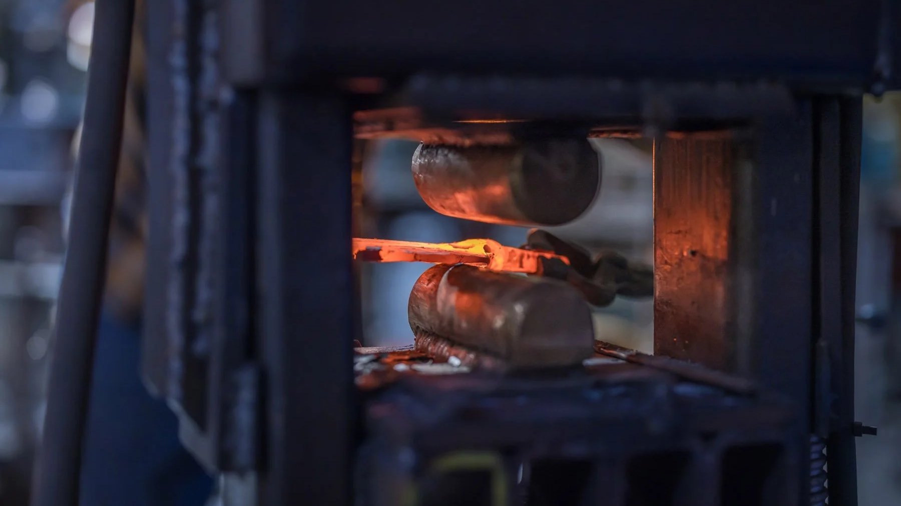 Industrial Photographer Richmond - An industrial photographer in Richmond captures a glowing heated metal bar pressed by rollers inside a forging machine.