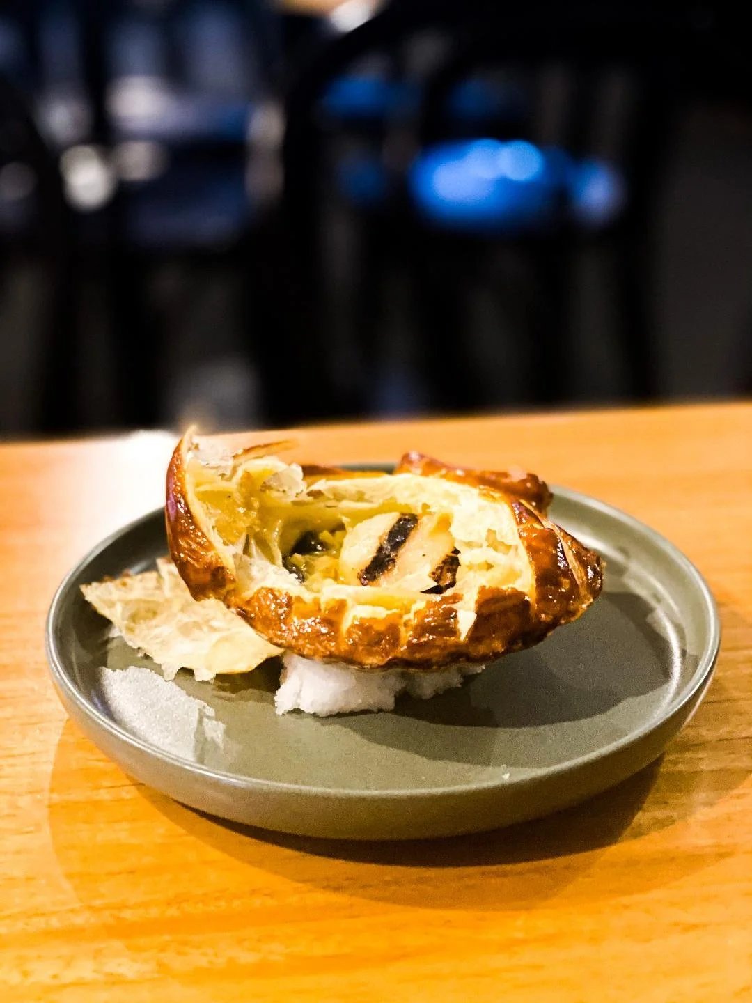 A partially eaten roasted chicken pot pie on a round gray plate placed on a wooden table, with a dark, blurry background.