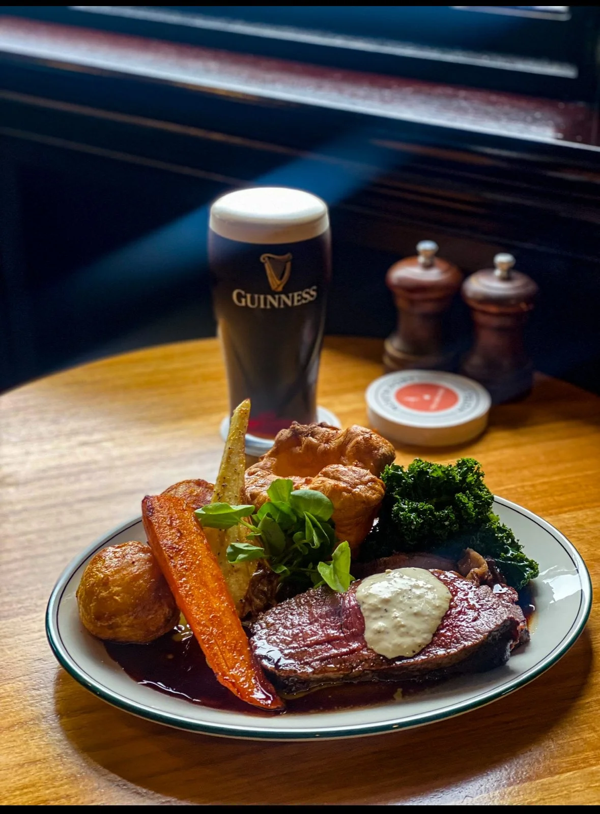A plate of traditional Irish food including roast beef, vegetables, and mashed potatoes, with a pint of Guinness beer in the background on a wooden table.