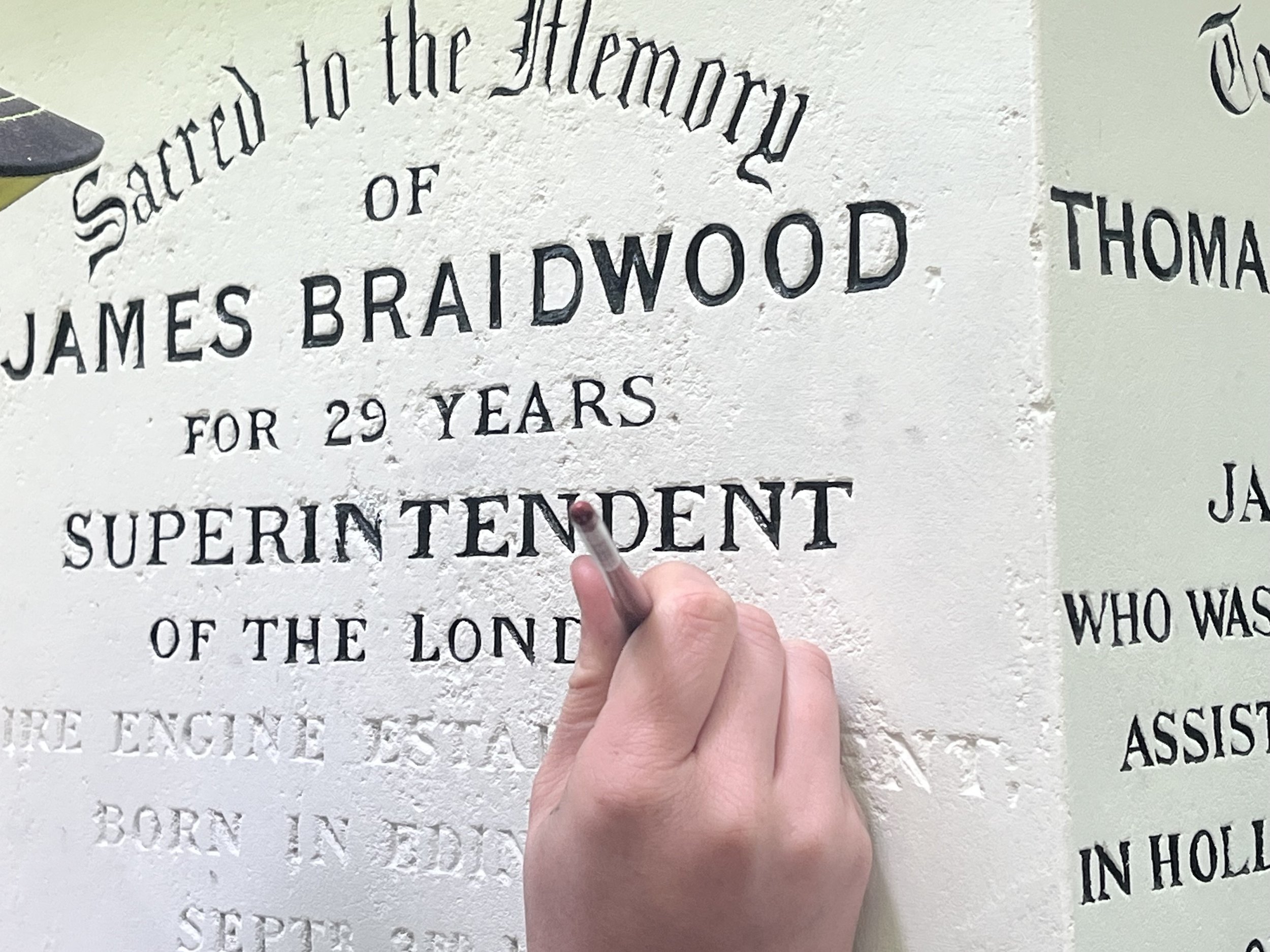 a hand carefully restores writing on a memorial