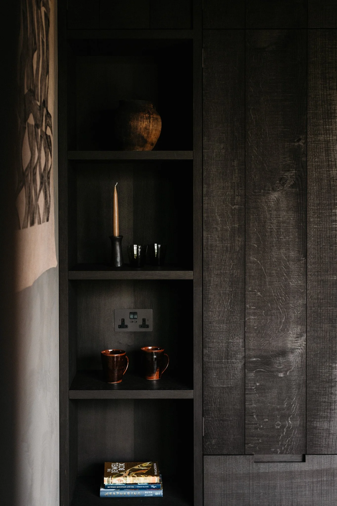 Dark wooden built-in bookshelf with decorative items and books inside, located next to a matching dark wooden wall panel.