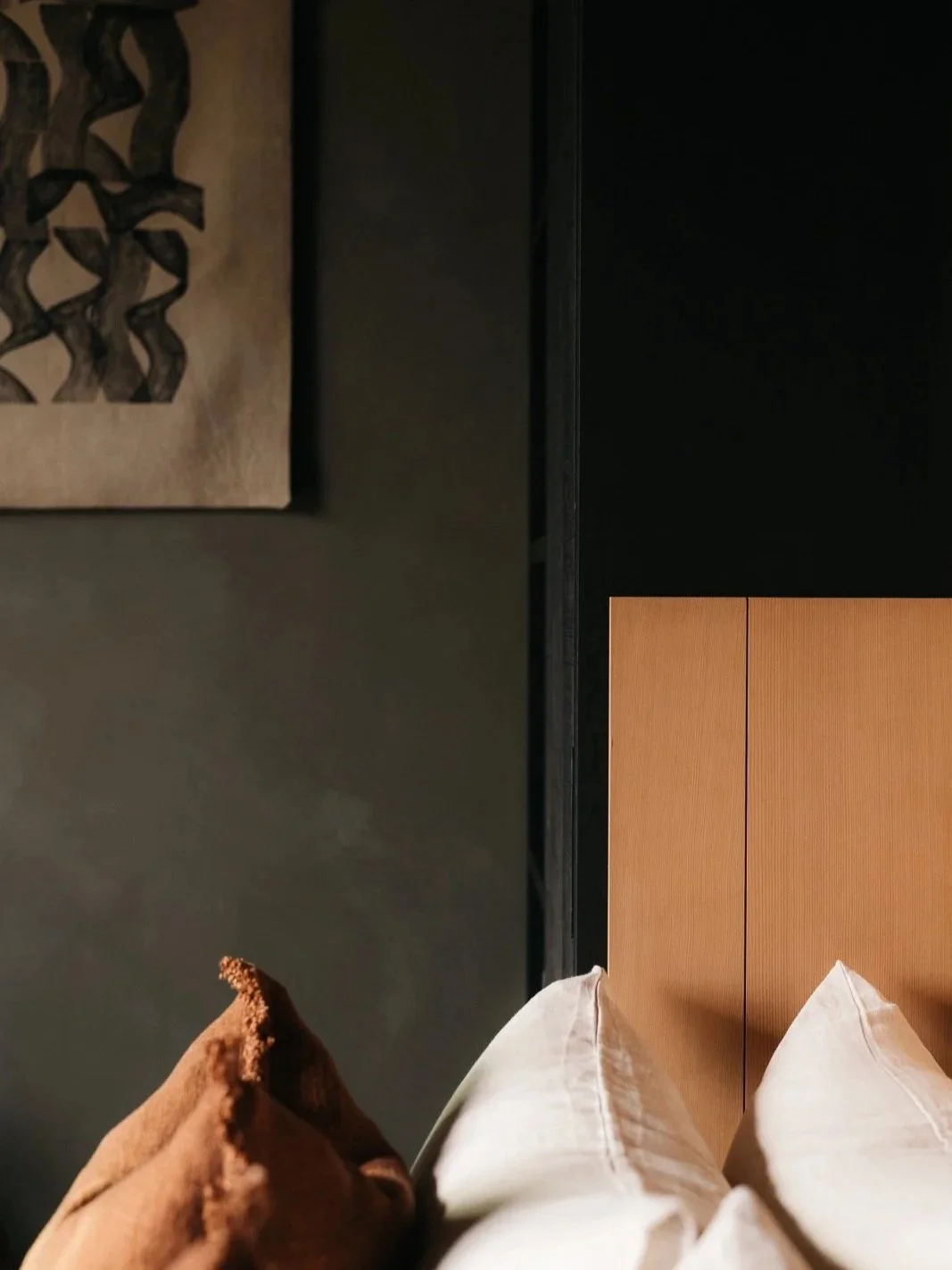 Part of a bedroom with a bedside table, two pillows on a bed, and a wall with a piece of artwork.