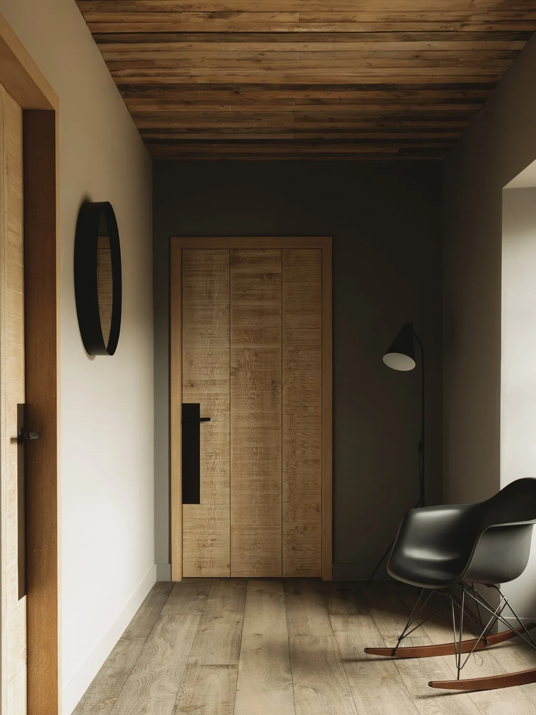 A room with wooden ceiling and floor, a wooden door, a black chair, a lamp, and a mirror on the wall.