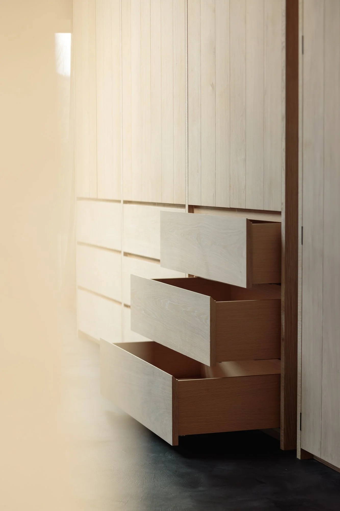 A wooden wardrobe with three open drawers in a minimalist room.