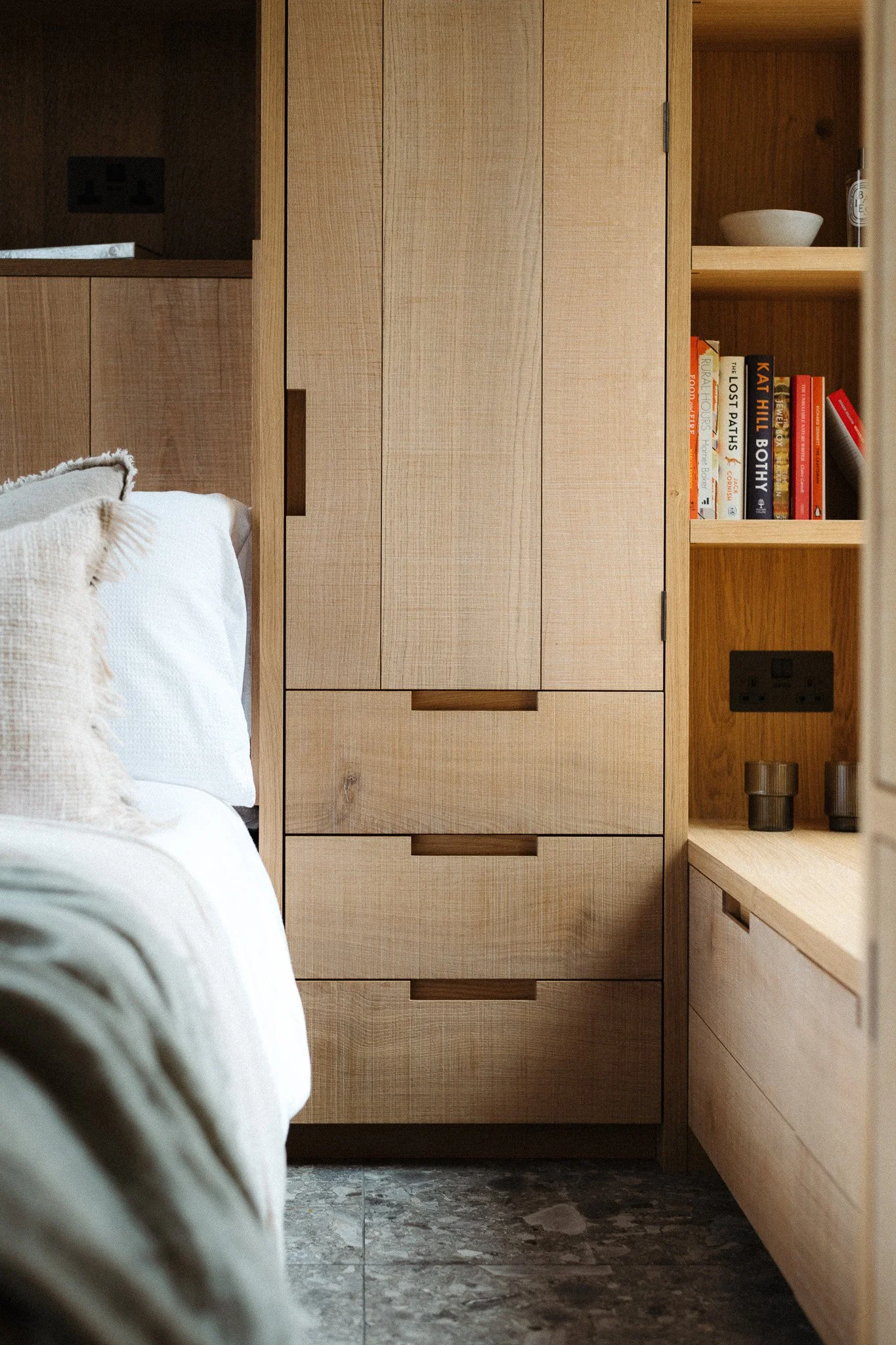 Close-up of a wooden wardrobe with drawers next to a bed and a bookshelf filled with books.