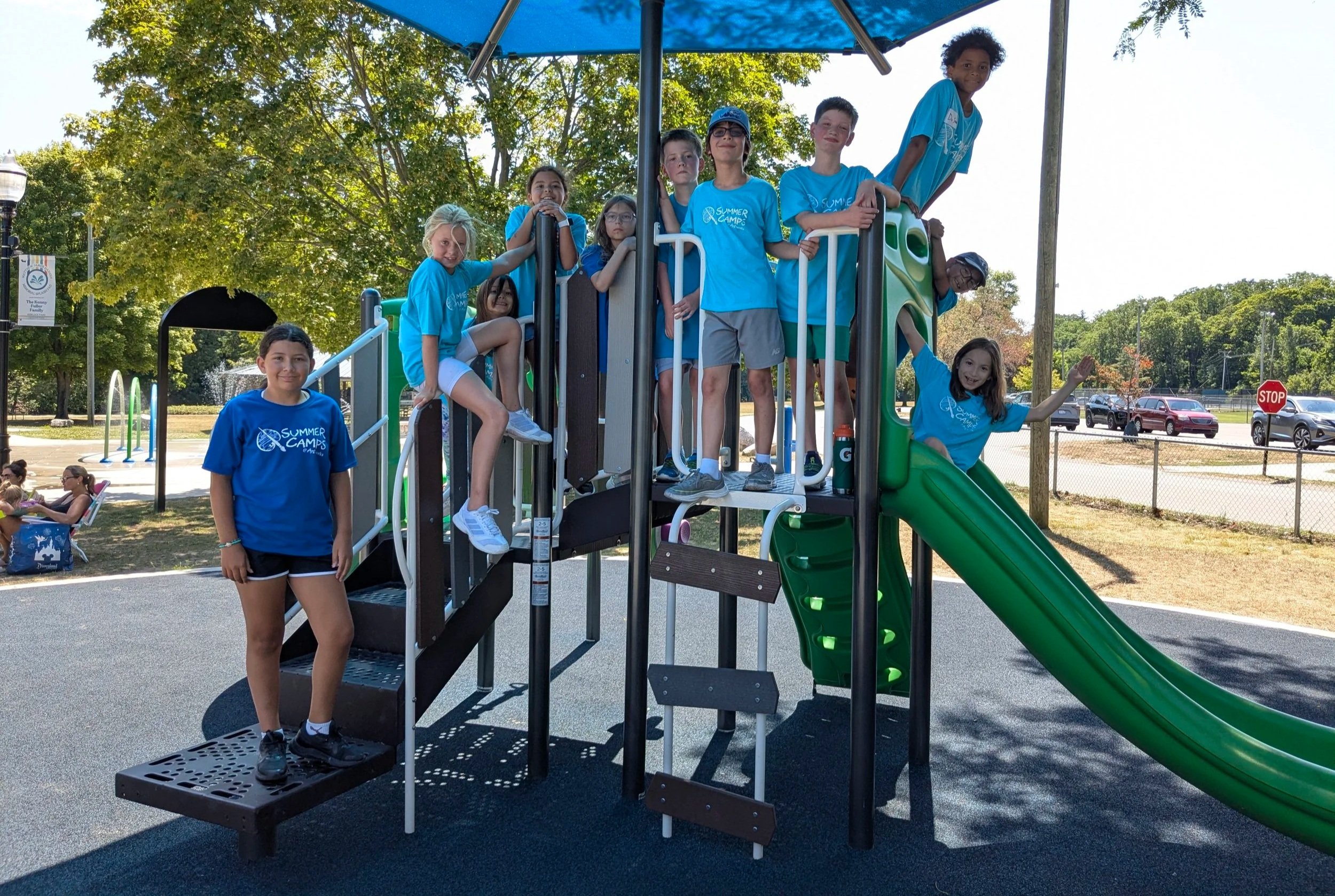 A group of summer camp participants smile on a slide at the local park