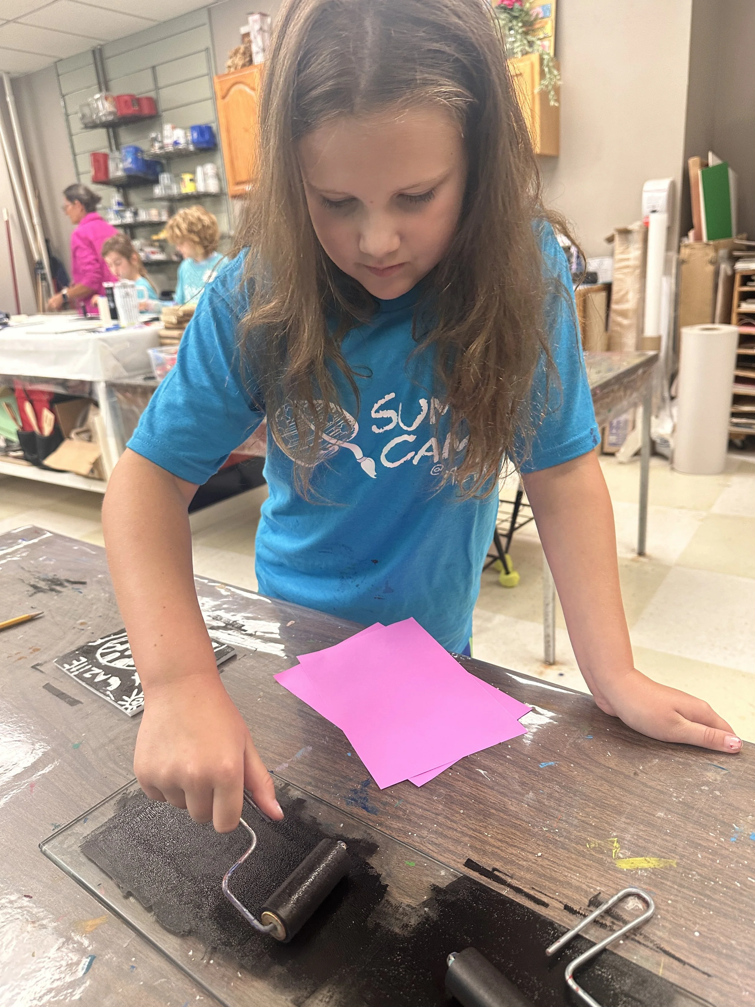 A summer camp participant spreads ink on a wooden block