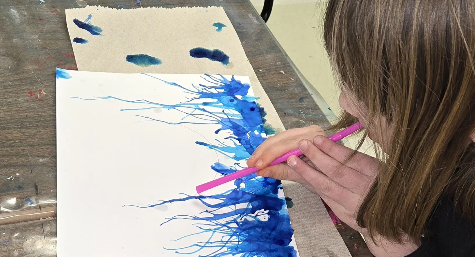 A young girl blows paint through a straw to create a drip painting