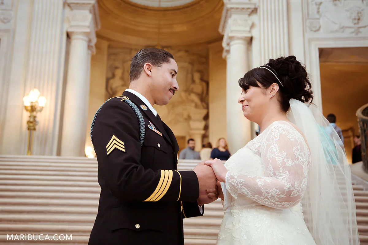 Bride and groom are holding hands and looks each other in the stairs and white architecture background of San Francisco City Hall