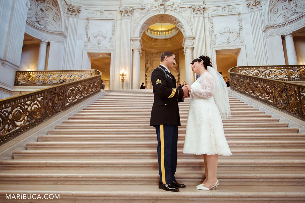 The bride and the groom are looking each other and smile in the staircase before wedding ceremony in the San Francisco City Hall