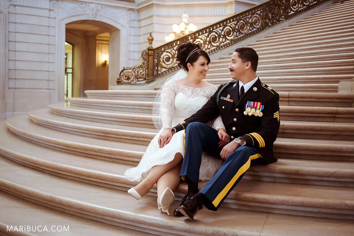The bride and the groom are sitting in the staircase and laugh each other in the SF City Hall wedding.