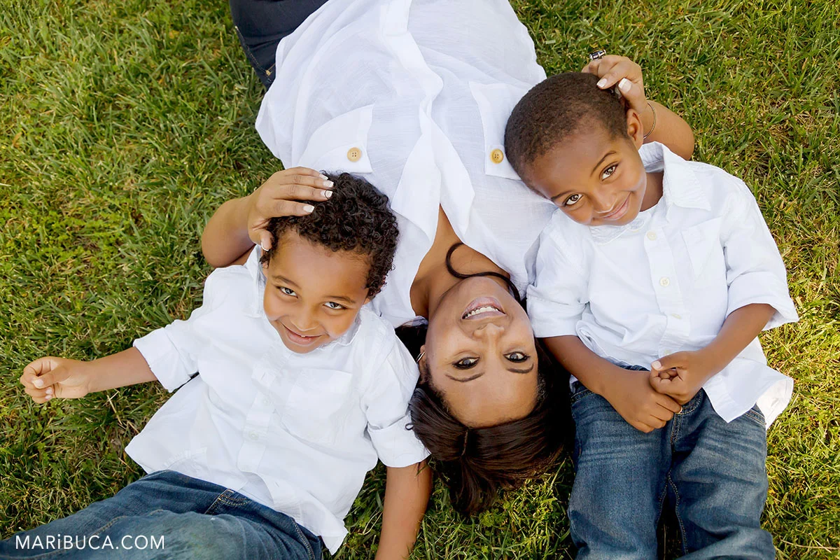 mom and her sons lay down in the grass. Family smiling.