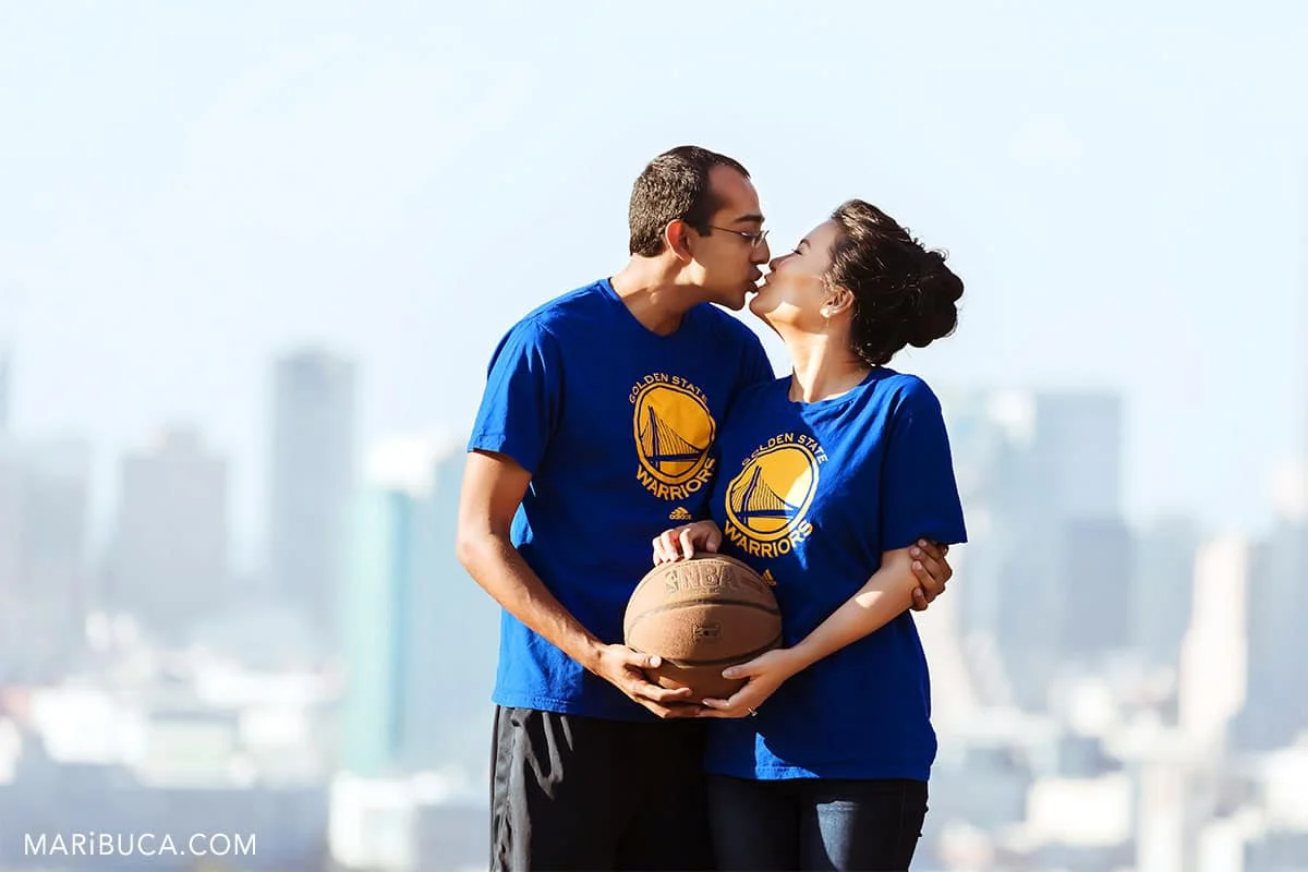 fiancee and fiance kissing and holding basketball.