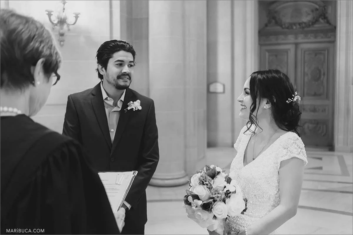 The black and white image. The groom and the bride are looking each other in the wedding ceremony in the SF City Hall
