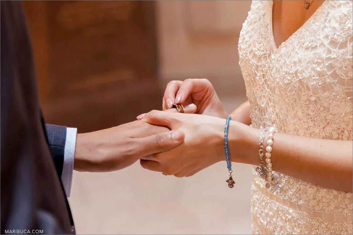 The bride in the white wedding dress and the groom in the blue jacket exchange the rings during wedding ceremony in the SF City Hall.