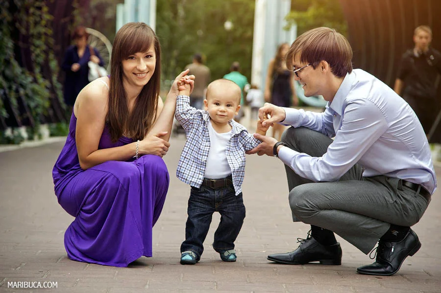 parents squatted down so that their baby son could stand comfortably and walk in the park