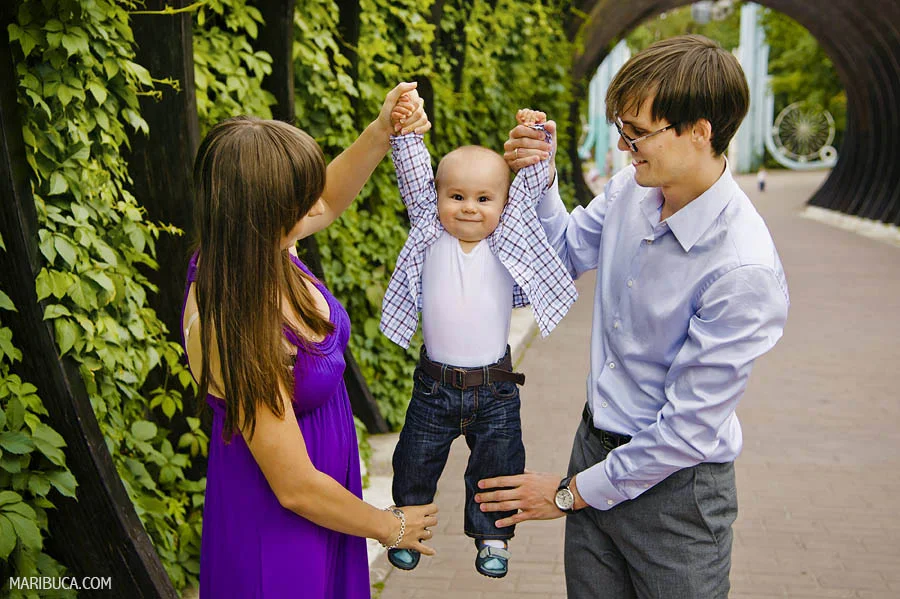 Parents holds his a little and adorable son and looks at him in the park