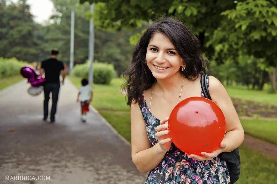 The lady is smiling and holding the red ball and her husband and son are leaving the park.