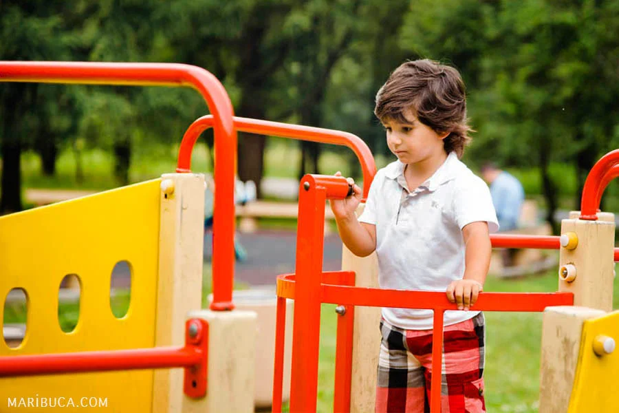 A boy in a white shirt and in red with black shorts is playing on a yellow ship in a children's wear area.