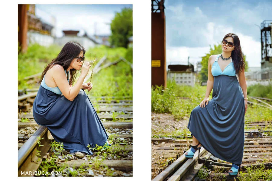 The girl in the blue dress and sunglasses posing against the backdrop of the old rail and industrial site