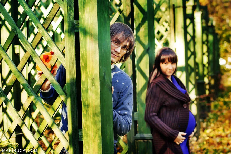 A pregnant girl and her husband are lying on the background of a decorative green fence in San Francisco