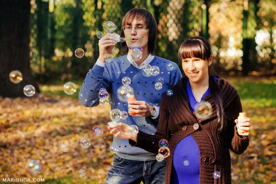 Newlyweds expect the first baby and have fun on the street in sunny autumn weather launching soap bubbles.