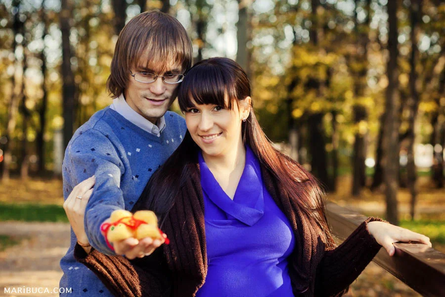Newlyweds stand hugging each other and hold yellow baby booties