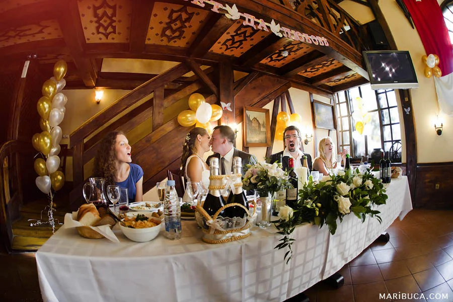 Just married couple around wedding party sit in the table in the barn.