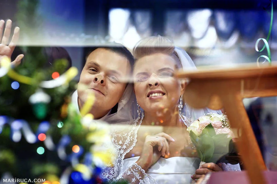 The groom and the bride make silly faces using the window in the shopping mall, San Jose.