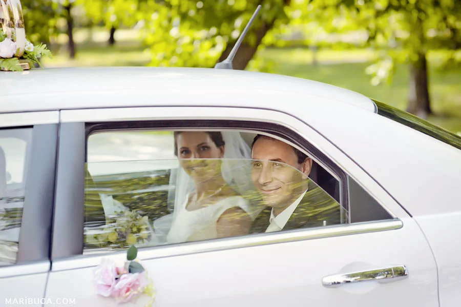 the bride and groom are sitting in a white car with the window ajar and smiling