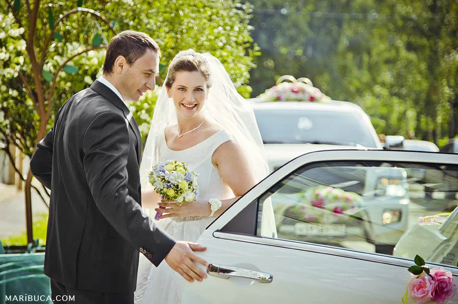 the groom opened the car door for the bride, the happy bride stands next to the groom in front of the registry office.