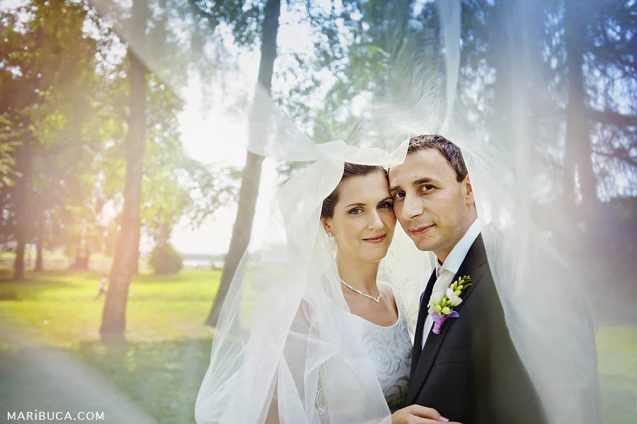 Bride and groom covered a white veil and the green garden as the background.