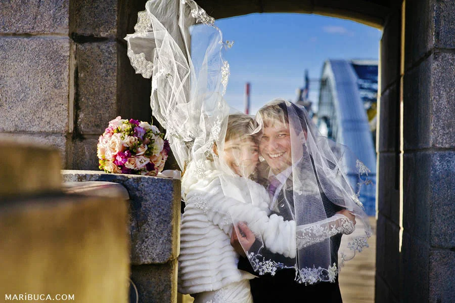 The bride and groom are covered with veils and part of the veil develops from the wind.