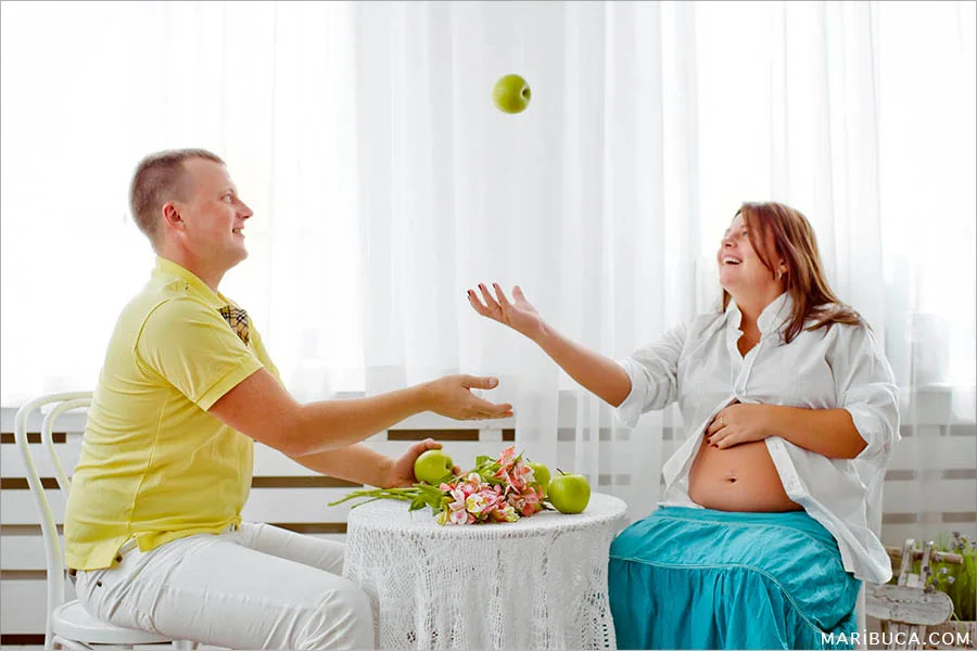 Maternity photographing a girl throws up green apples and a young man catches them