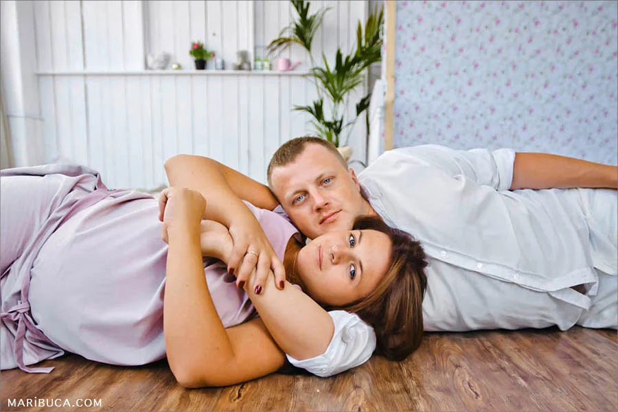 Girl and guy are expecting the baby hug each other and lay down in the hard floor.